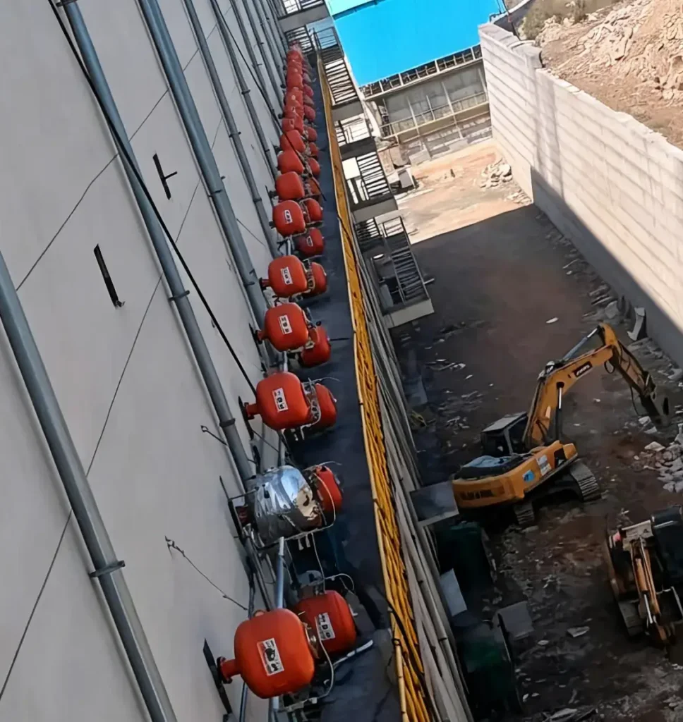 On-site industrial application featuring a multi-unit array of orange air cannons mounted along the exterior wall of a large storage silo to prevent material bridging and rat-holing.
