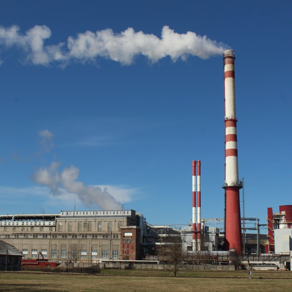 A large industrial factory with tall chimneys emitting smoke under a clear blue sky.